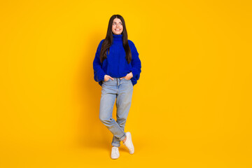 Fototapeta premium Smiling young woman wearing casual blue sweater against vibrant yellow backdrop exuding charm