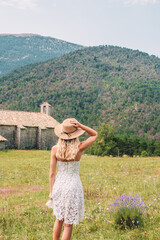 Young Blonde haired Woman in white dress walking on the green grass of Southern France, in front of Mountains