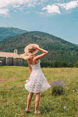 Young Blonde haired Woman in white dress walking on the green grass of Southern France, in front of Mountains