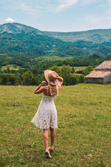 Young Blonde haired Woman in white dress walking on the green grass of Southern France, in front of Mountains