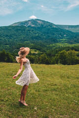 Young Blonde haired Woman in white dress walking on the green grass of Southern France, in front of Mountains
