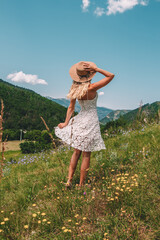 Young Blonde haired Woman in white dress walking on the green grass of Southern France, in front of Mountains