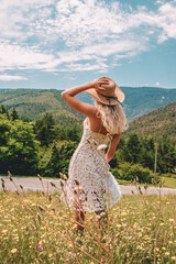 Young Blonde haired Woman in white dress walking on the green grass of Southern France, in front of Mountains
