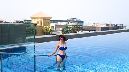 Woman hat exits swimming pool holding handrail.