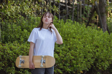 Portrait of teenage girl holding skateboard in white t-shirt with her hair down on green background.
