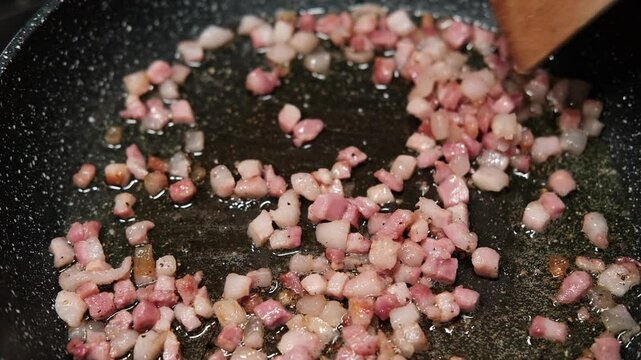chef roasts cubes of bacon or Italian pork guanciale or pancetta in a pan for Italian pasta carbonara , A woman cooking Italian spaghetti carbonara pasta 