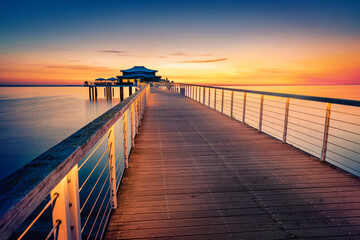 Fototapeta premium Dramatic morning seascape of Baltic sea. Calm summer sunrise on Wolkenlos Timmendorfer Strand illuminated pier, Germany, Europe. Traveling concept background.