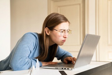 Woman with poor eyesight wearing eyeglasses looking too close at laptop screen at desk during work...