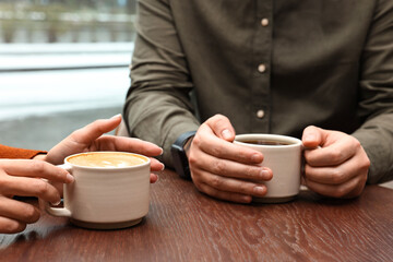 Colleagues having coffee break at wooden table in cafe, closeup