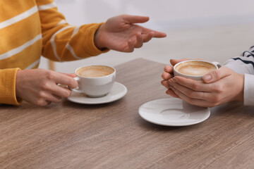 Coffee break. Women with cups of hot drinks at wooden table indoors, closeup