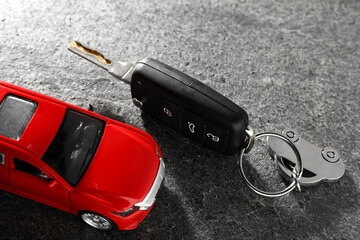 Car key and model on grey textured table, closeup. Buying auto