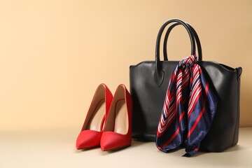 Leather bag with handkerchief and high heeled shoes on beige background. Space for text
