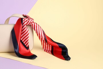 Handbag with striped scarf on color background. Space for text