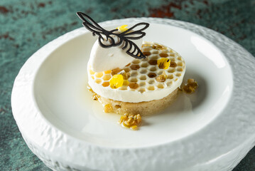 An elegant dessert featuring honeycomb, creamy mousse, and garnished with edible flowers, beautifully presented on a textured white plate.