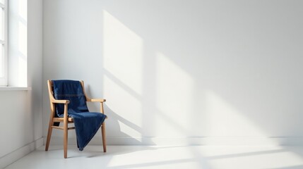 A wooden chair draped with denim fabric sits near a bright window in a minimalist room, bathed in sunlight.