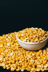 Portrait of Organic Bengal Gram (Cicer arietinum) placed in a ceramic white bowl, with split yellow chana dal forming the gradient background.