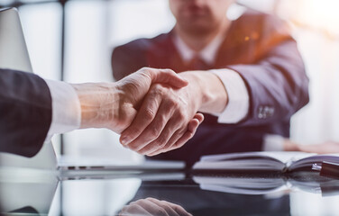 Close-up high-angle view of unrecognizable business men handshaking after close deal and signed agreement at office over table paper contract.