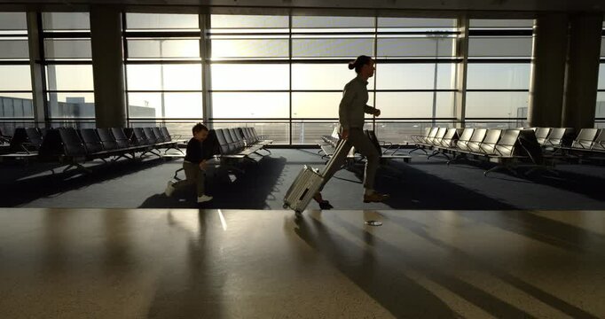 Father pulling rolling suitcase run to boarding gate, followed by little boy, slow motion shot at empty and big modern terminal. High contrast shot, bright sun shine through big windows