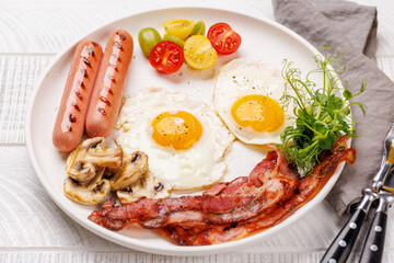 A classic breakfast plate featuring sunny-side-up eggs, crispy bacon, sausages, and fresh tomatoes