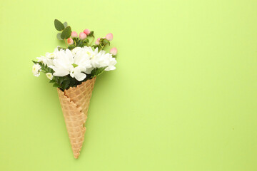 Waffle cone with chamomile flower, leaves on beige background. Flat lay, top view floral background.