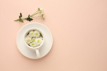 White coffee cup with white flowers spilling out of it on a beige background, spring mood