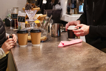 A bartender at a cafe behind the counter prepares a customer's takeaway coffee
