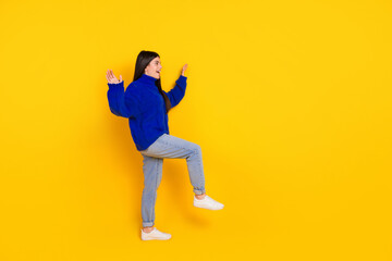 Fototapeta na wymiar Cheerful young woman in a blue sweater gesturing playfully against a vibrant yellow background
