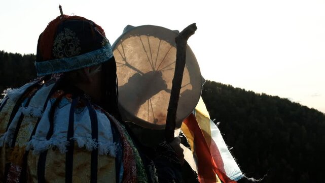 Shaman holding drum and prayer flags at sunset