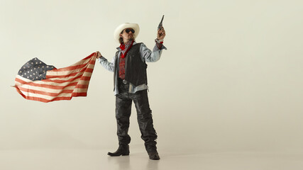 Powerful cowboy in white hat and leather vest, pointing revolver forward, gripping American flag,...