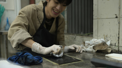 A Close-up image of a printmaker carefully wiping an etching plate with a cloth, ensuring the right...