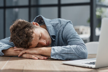 Fototapeta premium young office man at a laptop sleeping at his workplace