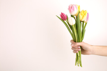 Woman holding bouquet of beautiful spring tulips and text 8 March on light background, closeup. International Women's Day