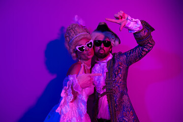 Couple in historic costumes at neon-lit party backdrop exuding vintage charm and playful...