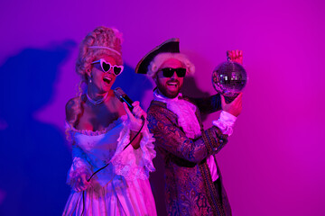 Couple in historical-themed costumes enjoying a lively neon party with a disco ball and vibrant...