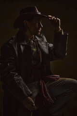 Mysterious man, cowboy adjusting hat, dressed in leather coat, exuding silent strength and wisdom against moody background. Concept of resilience, frontier survival, western history.