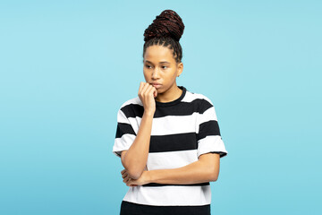 Young woman with braids looking pensive with hand on chin against blue background