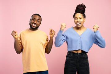 Overjoyed couple celebrating success with raised fists on pink background