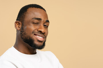 Young african american man winking and smiling on beige background
