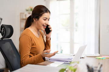 Businesswoman talking on smartphone. Happy female small Business entrepreneur is wearing casual. She is working with laptop computer in cozy living room at home.