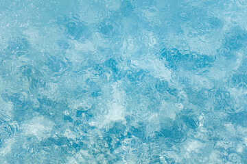 Obraz premium Clear blue water surface with ripples and raindrop circles creating abstract patterns. Sunlight reflections and transparency enhance the dynamic texture of the liquid background. 