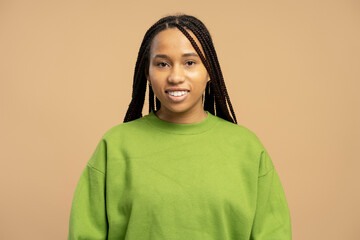 Fototapeta premium Young woman smiling wearing green sweater and braided hair on beige background