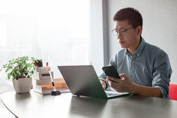 asian businessman using smart phone and laptop in office