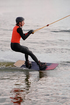 А girl riding a wakeboard on a calm water surface in cloudy weather