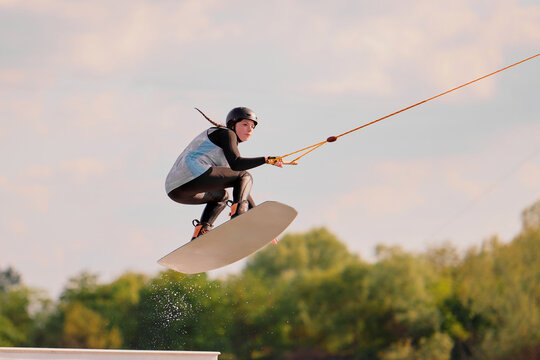 A wakeboarder mid-air performing a trick, with a clear sky in the background. The scene captures the thrill and skill of the sport