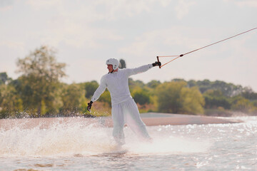 A person in white attire wakeboarding on a lake, creating a spray of water.