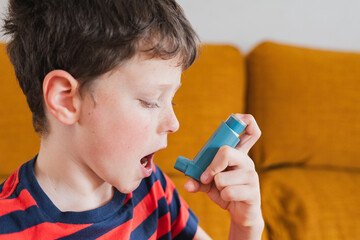 Young boy using an inhaler for asthma relief in a cozy living room
