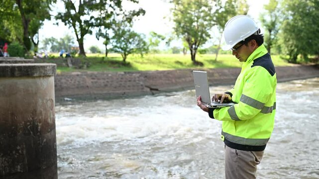 A engineering doing his checking routine. He is wearing hard hat and engineer uniform.Standing by the rail by the dam.Monitor water levels from the heavy rain that has been falling for several days.