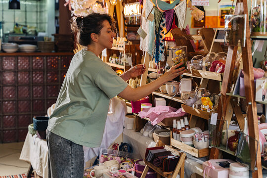 Artisan organizing handcrafted decor at a market stall. Variety of handmade crafts and decorations at local fair.