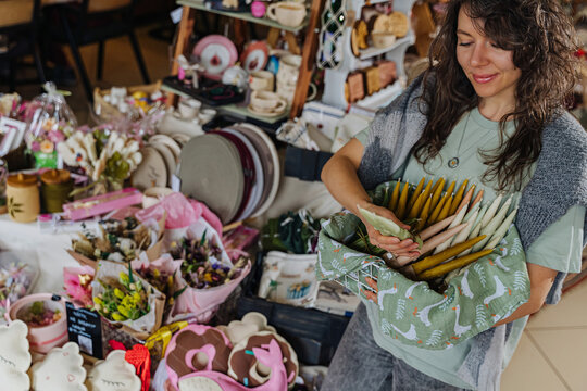 Artisan organizing handcrafted decor at a market stall.  Colorful handmade candles, flowers, and decor at craft fair.