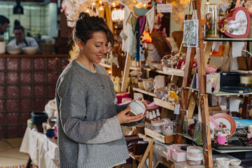 Woman shopping for unique handmade items at craft fair. Variety of handmade crafts and decorations at local fair.